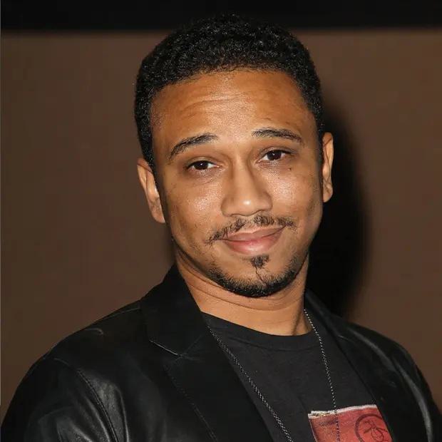 light-skinned black man with a slight smile and close-cropped hair, moustache and goatee