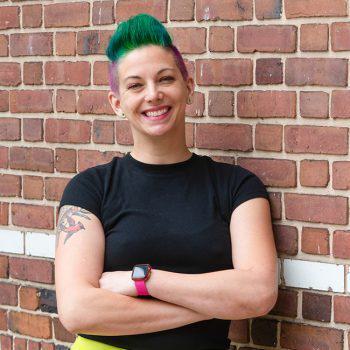 Smiling woman with green spiky short hair and a visible upper arm tattoo