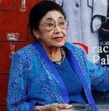 elderly latina woman with very dark here captured in mid-sentence and holding a book